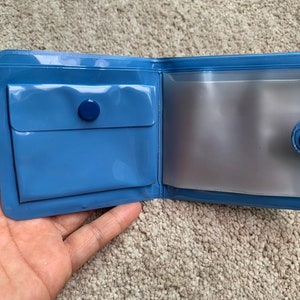 May include: A blue vinyl wallet with a clear plastic window and a snap closure.