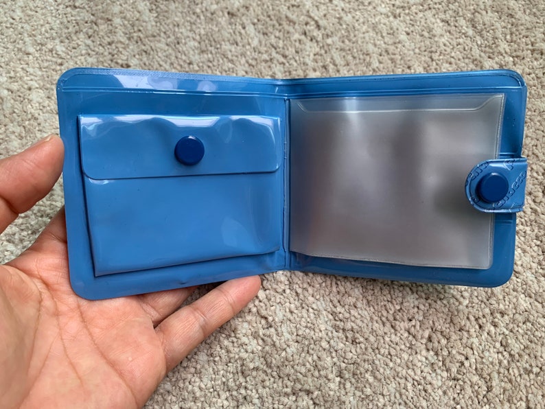 May include: A blue vinyl wallet with a clear plastic window and a snap closure.