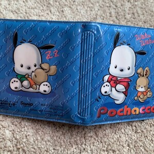 May include: A blue and white wallet with a cartoon dog and rabbit design. The wallet has the text "Pochacco" and "Waku Waku" on it.
