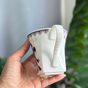 May include: White ceramic teacup with a brown and white floral design and a handle with small heart details.