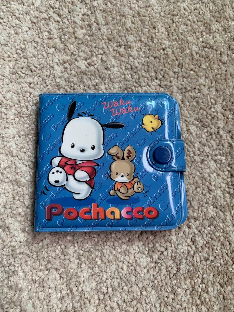 May include: A blue wallet with a cartoon character named Pochacco. The wallet has a snap closure and features the text "Waku Waku" and "Pochacco" in a colorful font.