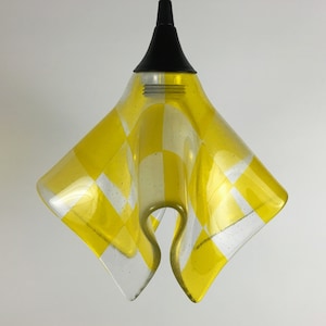 May include: A yellow and white checkered glass pendant light fixture with a black metal hanging cord.