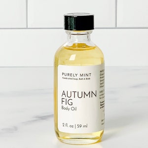 Organic Vegan Body Oil: Nut-Free, Sensitive Skin, Natural Moisturizer in a clear glass bottle with a black lid lled with Autumn Fig body oil. The bottle is labeled 'PURELY MINT Handcrafted Soap, Bath & Body AUTUMN FIG Body Oil 2 fl. oz | 59 ml'