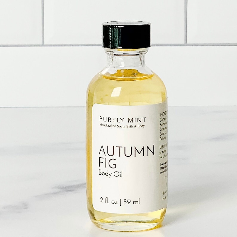 Organic Vegan Body Oil: Nut-Free, Sensitive Skin, Natural Moisturizer in a clear glass bottle with a black lid lled with Autumn Fig body oil. The bottle is labeled 'PURELY MINT Handcrafted Soap, Bath & Body AUTUMN FIG Body Oil 2 fl. oz | 59 ml'