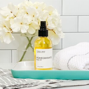 Organic Vegan Body Oil: Nut-Free, Sensitive Skin, Natural Moisturizer. A clear glass bottle with a black pump top filled with yellow body oil. The bottle is sitting on a light blue tray with a white towel next to it.