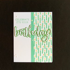 May include: A white card with green and yellow accents. The card says "Celebrate it's your birthday" with the word "birthday" in a large, green, cursive font.