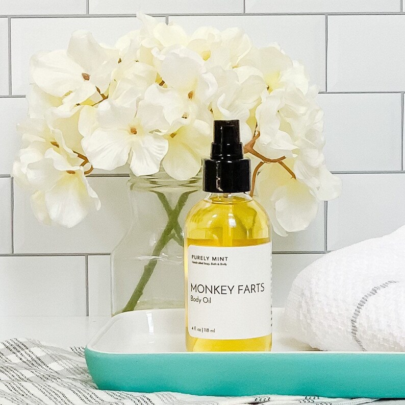 Organic Vegan Body Oil: Nut-Free, Sensitive Skin, Natural Moisturizer. A clear glass bottle with a black spray nozzle and a white label. The bottle is sitting on a teal tray with a white towel behind it.