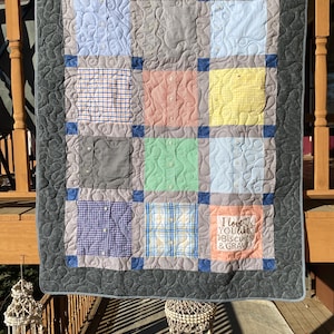 Könnte beinhalten: Eine graue und blaue Patchwork-Decke aus wiederverwendeten Hemden. Die Decke ist mit einem Wirbelmuster gesteppt und hat ein quadratisches Design mit 12 Quadraten. Das mittlere Quadrat hat eine gestickte Botschaft mit dem Text "Ich liebe dich wie Biscuits & Gravy".