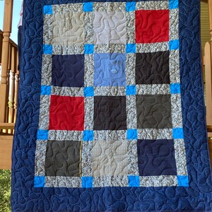 Könnte beinhalten: Eine blaue und weiße Patchwork-Decke mit verschiedenen Stoffen, darunter Denim, Flanell und Baumwolle. Die Decke ist mit einem blauen Rand eingefasst.