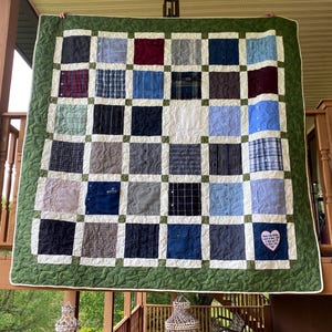 Könnte beinhalten: Eine grüne Patchwork-Decke aus wiederverwendeten Hemden. Die Decke besteht aus 36 Quadraten, jedes mit einem anderen Muster. Die Decke hat einen weißen Rand und einen grünen Außenrand. Die Decke hat einen rosa herzförmigen Patch mit dem Text "Jeder Stich eine Erinnerung, jeder Knopf ein Lächeln, ich werde immer bei dir sein, Papa."