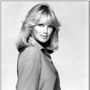 Puede incluir: Retrato en blanco y negro de una mujer con cabello rubio, vestida con una camisa con cuello y pantalones. La mujer mira hacia la cámara con una ligera sonrisa. La imagen es una toma de estudio.