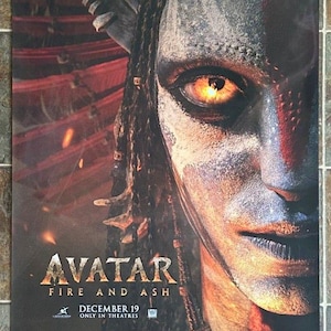 May include: Poster for the movie "Avatar: Fire and Ash" featuring a close-up of a Na'vi character's face. The poster has a dark color scheme with the movie title and release date, December 19, displayed prominently.