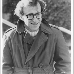 Könnte beinhalten: Schwarz-Weiß-Werbefoto aus dem Film "Broadway Danny Rose". Das Bild zeigt einen Mann mit Brille, Mantel und Pullover. Der Filmtitel und die Copyright-Informationen befinden sich unten.