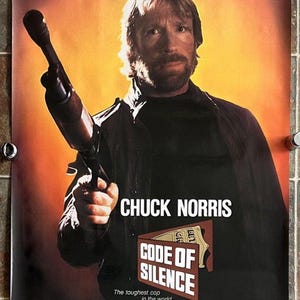 May include: Film poster for "Code of Silence" starring Chuck Norris. The poster shows Norris holding a gun, with the film's title and tagline: "The toughest cop in the world... just got tougher."