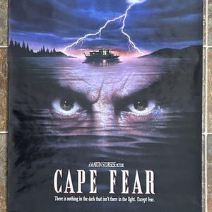 May include: Cape Fear movie poster featuring Robert De Niro, Nick Nolte, and Jessica Lange. The poster shows a boat on water with a lightning strike and the eyes of a person in the water. The text "CAPE FEAR" is prominently displayed.