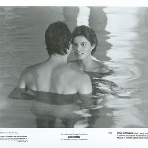 May include: A black and white photo of a couple in a swimming pool. The man is in the foreground and the woman is in the background. The man is looking at the woman and the woman is looking at the camera. The photo is from the movie "Cocoon".