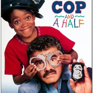 May include: Movie poster for the film "Cop and a Half" starring Burt Reynolds and Ruby Dee. The poster features a close-up of Burt Reynolds and Ruby Dee, with Ruby Dee wearing a police officer's hat and holding handcuffs over Burt Reynolds' eyes. The poster's title is "Cop and a Half" with the words "One kid's fantasy. One cop's nightmare." printed above the title.