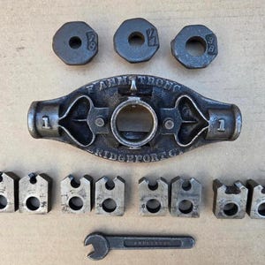 May include: A collection of vintage metal tools, including a central vise with the text "F. ARMSTRONG BRIDGEPORT CT" and several interchangeable parts. There are also three octagonal pieces and a small wrench.