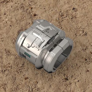 May include: A futuristic, silver-colored cylindrical device with intricate geometric designs and a ring-shaped component. The object has a metallic appearance and is set against a sandy, brown background.