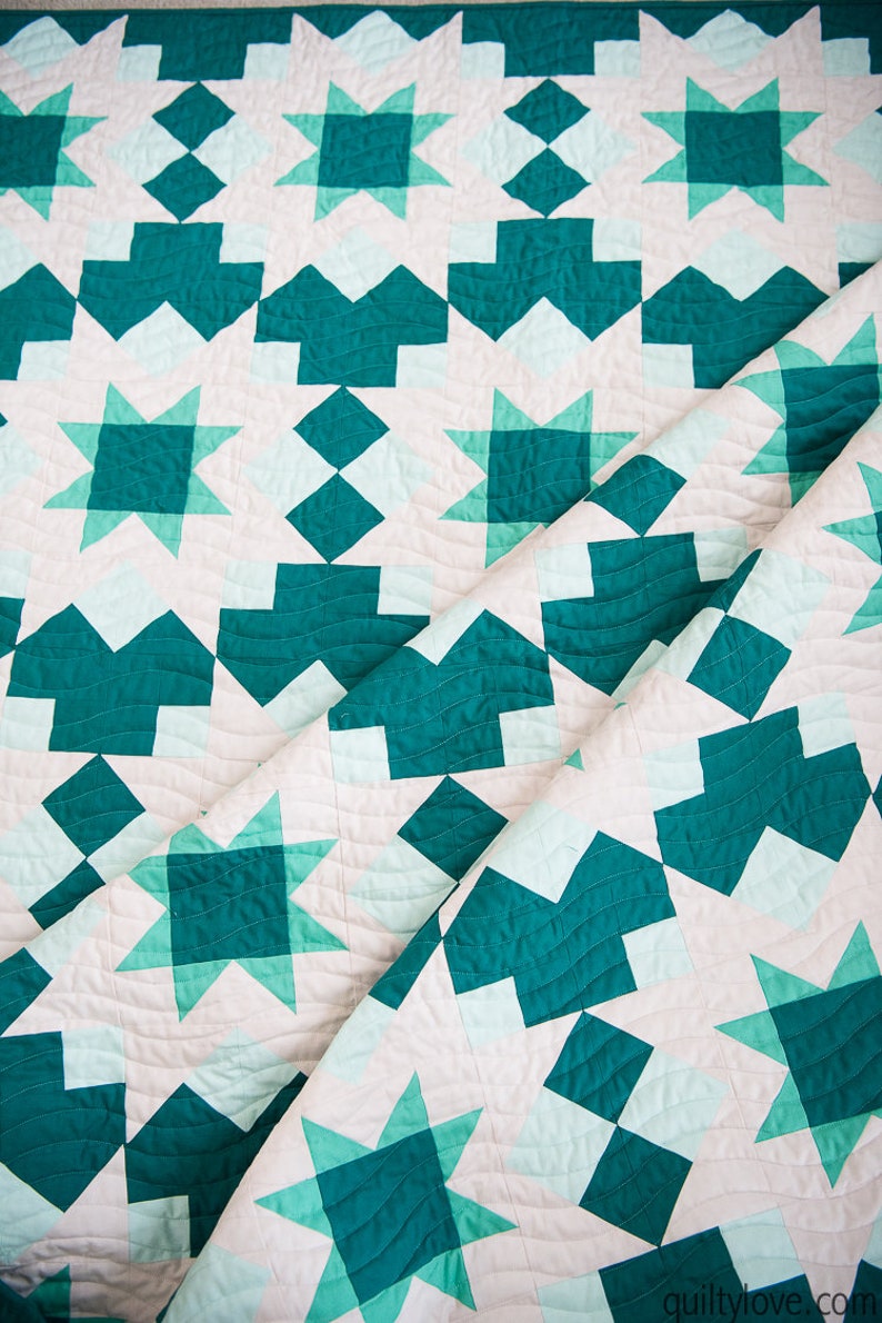 May include: A teal and white quilt with a geometric pattern of stars and squares. The quilt is folded in half, revealing the intricate stitching.