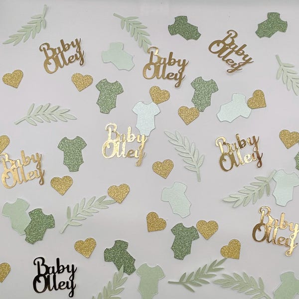 May include: Confetti for a baby shower, featuring gold glitter hearts, baby onesies in light green and glittery green, and leaf shapes. The words "Baby Olley" are in gold and black script.