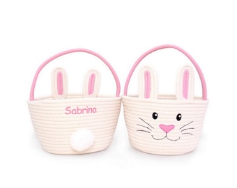 Può includere: Due cestini pasquali bianchi intrecciati con dettagli rosa. Un cestino ha un manico rosa, orecchie da coniglio e il nome "Sabrina" ricamato in rosa. L'altro ha un design a forma di coniglio con naso e baffi rosa.