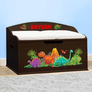 May include: A brown wooden toy chest with a white padded lid. The chest features a dinosaur theme with a volcano, palm trees, and five dinosaurs in green, orange, purple, and blue. The name "BRYSON" is written in red letters on the lid.