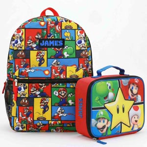 May include: A backpack and a rectangular lunch bag featuring a colorful Super Mario character print. The backpack has a black rectangular patch with the name JAMES in blue text. The lunch bag features a large yellow star and the name JAMES in blue.