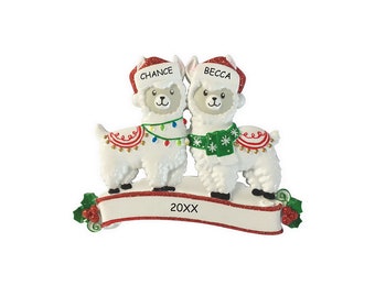 May include: A Christmas ornament featuring two white llamas wearing Santa hats and festive scarves. One llama has a string of lights, the other a green scarf. The banner below reads "20XX" and the names "Chance" and "Becca" are on the hats.
