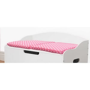 May include: White toy storage chest with a pink and white polka dot cushion on top. The chest has a black handle and a cutout on the side.