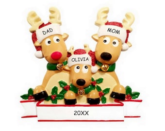 May include: A personalized Christmas ornament featuring a family of three reindeer. The reindeer are wearing Santa hats with the names "Dad", "Mom", and "Olivia" written on them. The ornament also includes a banner with the year "20XX" written on it.