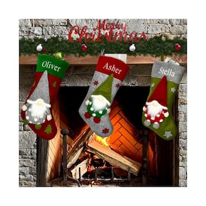 May include: Three Christmas stockings with gnome designs hang above a fireplace. Each stocking is personalized with a name: Oliver, Asher, and Stella. The stockings are red, gray, and green, with decorative elements and the words "Merry Christmas" above.