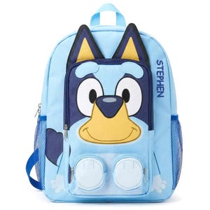 May include: Light blue backpack featuring a cartoon dog face with large eyes, a yellow nose, and a smiling mouth. The backpack has a top handle, side mesh pockets, and the name "STEPHEN" printed on the side.