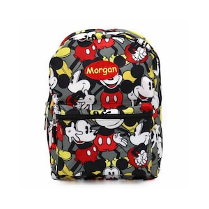 May include: A gray backpack featuring a repeating pattern of Mickey Mouse in red, black, white, and yellow. The backpack has a red patch with the name "Morgan" in white letters. It has a black zipper and a top handle.