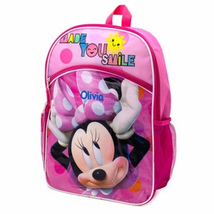 May include: Pink Minnie Mouse backpack with a large image of Minnie Mouse on the front. The backpack has a mesh pocket on the side and a zippered pocket on the front. The text "Made You Smile" is printed on the top of the backpack. The name "Olivia" is printed on the bow of Minnie Mouse.