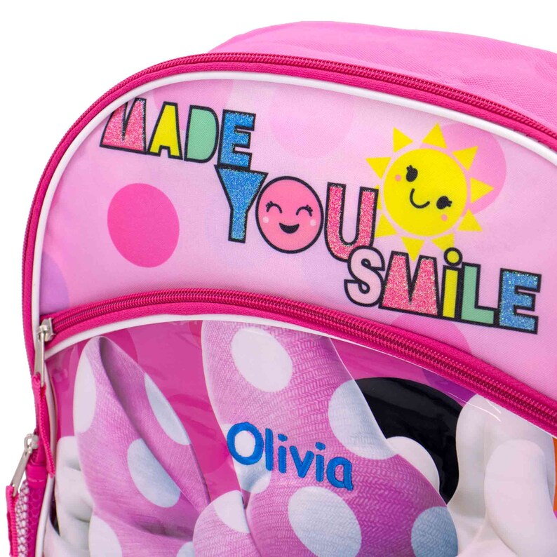 May include: Pink polka dot backpack with a clear front pocket featuring a cartoon image of Minnie Mouse. The backpack has a pink zipper and the text "Made You Smile" with a sun and smiley face graphic.