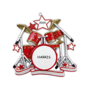 May include: Red and gold drum set Christmas ornament with a white banner that says "HARRIS" and a star with the year "20XX" on it.