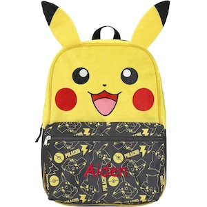 May include: Yellow Pikachu backpack with black accents, featuring Pikachu's face on the front. The lower section has a black pattern with Pikachu graphics and the name "Aiden" embroidered in red. Includes a top handle and adjustable straps.