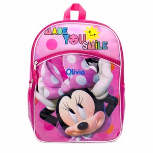 May include: Pink Minnie Mouse backpack with a clear front pocket featuring a pink bow and the name "Olivia". The backpack has a white zipper and the text "Made You Smile" with a yellow sun graphic.