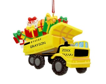 May include: Yellow toy dump truck Christmas ornament with a red ribbon, filled with colorful wrapped presents. The truck has the name "GRAYSON" and the year "20XX" printed on it.