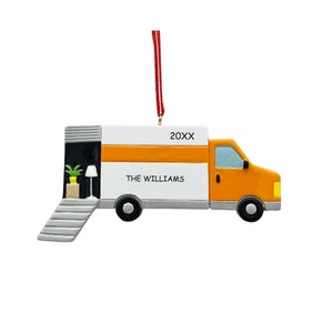 May include: A white and orange moving truck Christmas ornament with a gray ramp and a small house inside. The truck has the text "THE WILLIAMS" and "20XX" on the side.