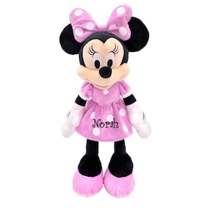 May include: Pink plush Minnie Mouse doll with white polka dots and a black bow. The doll is wearing a pink dress with white polka dots and the name "Norah" embroidered on the front.
