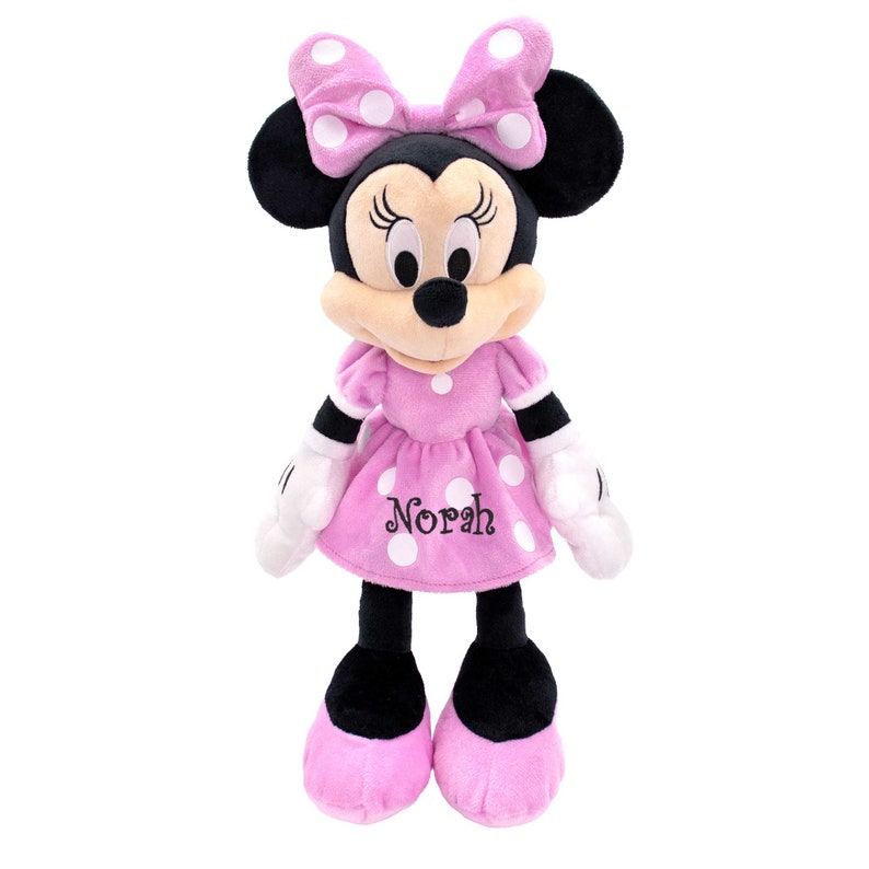 May include: Pink plush Minnie Mouse doll with white polka dots and a black bow. The doll is wearing a pink dress with white polka dots and the name "Norah" embroidered on the front.