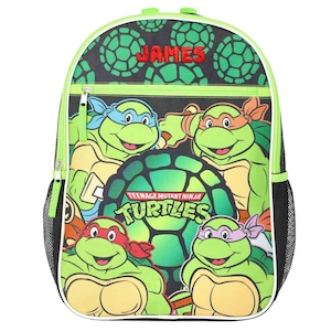 May include: A black backpack featuring a Teenage Mutant Ninja Turtles graphic with four turtles wearing colored masks. The name JAMES is embroidered in red at the top. The bag has a lime green trim, a front zippered pocket, and black mesh side pockets.
