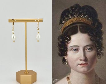 May include: Gold hoop earrings with a teardrop-shaped pearl pendant. The earrings are displayed on a gold stand.