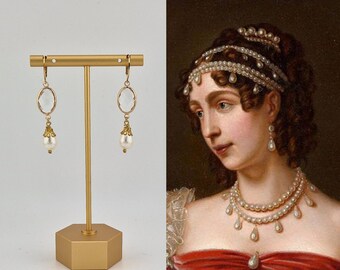 May include: Gold-toned earrings with a clear, oval-shaped stone and a dangling white pearl. The earrings are displayed on a gold stand. The image also features a portrait of a woman wearing similar pearl jewelry.