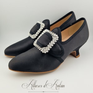 May include: Black satin heeled shoes with a large, jeweled buckle. The buckle is made of silver metal and has a large, round, clear rhinestone design.
