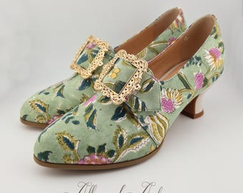 Puede incluir: Un par de zapatos de tacón verde con estampado floral y detalles de hebilla dorada. Los zapatos tienen punta puntiaguda y un tacón bajo de bloque.