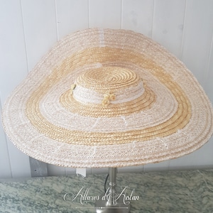 May include: A large, wide-brimmed straw hat with a white lace trim and delicate yellow flowers. The hat is a light beige colour and has a wide, flat brim.