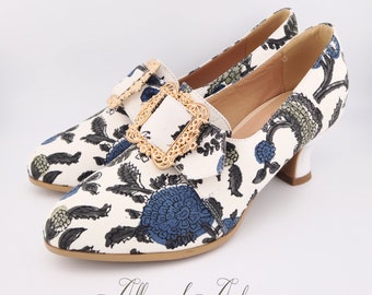 Puede incluir: Zapatos de tacón blanco con estampado floral con flores azules y verdes. Los zapatos tienen una hebilla dorada con un diseño ornamentado.